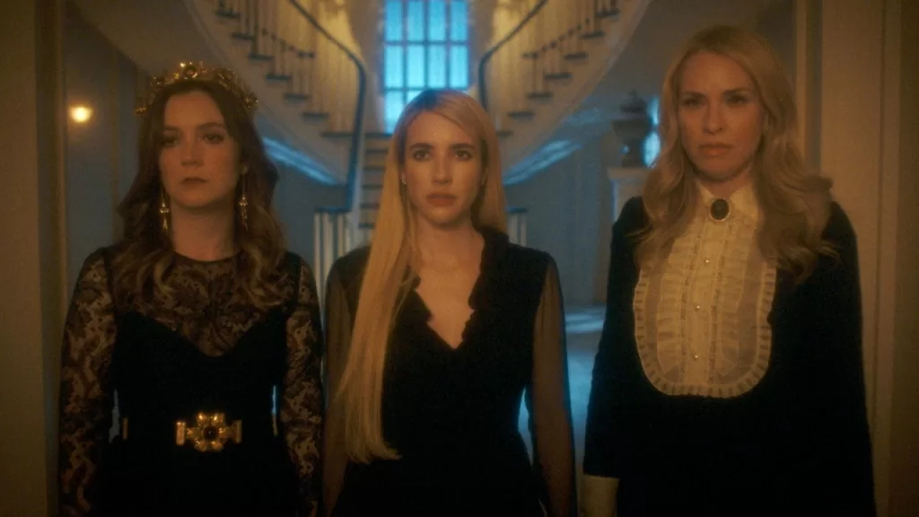 Três bruxas vestidas de preto no saguão de uma mansão, em cena da 13ª temporada de American Horror Story