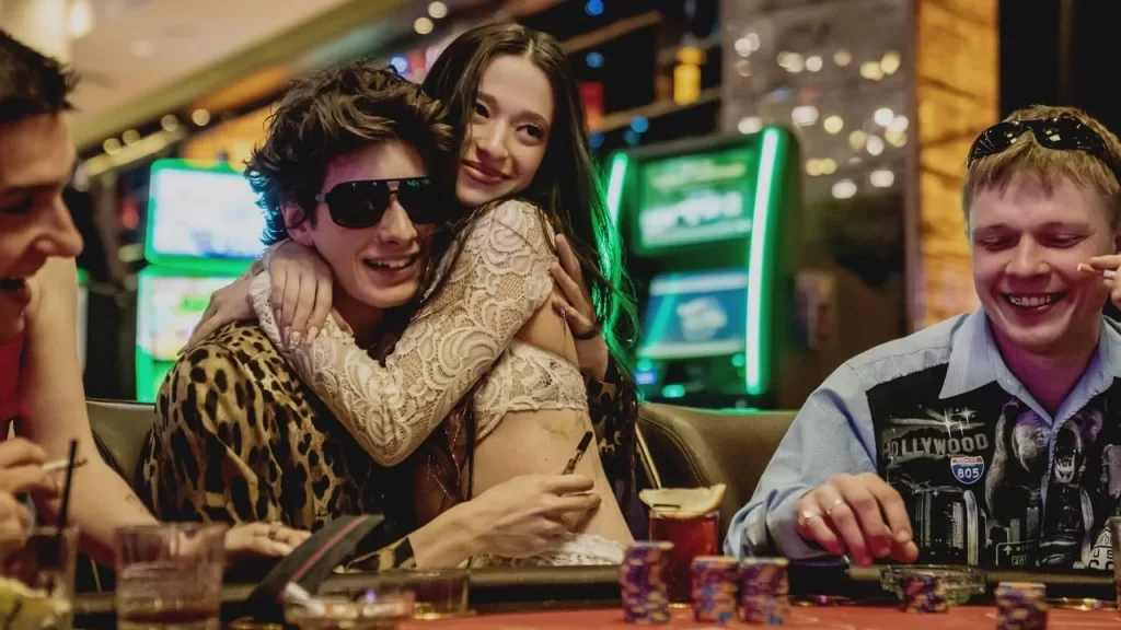 Mikey Madison como Anora abraçada a Mark Eydelshteyn em um cassino, ao lado de amigos