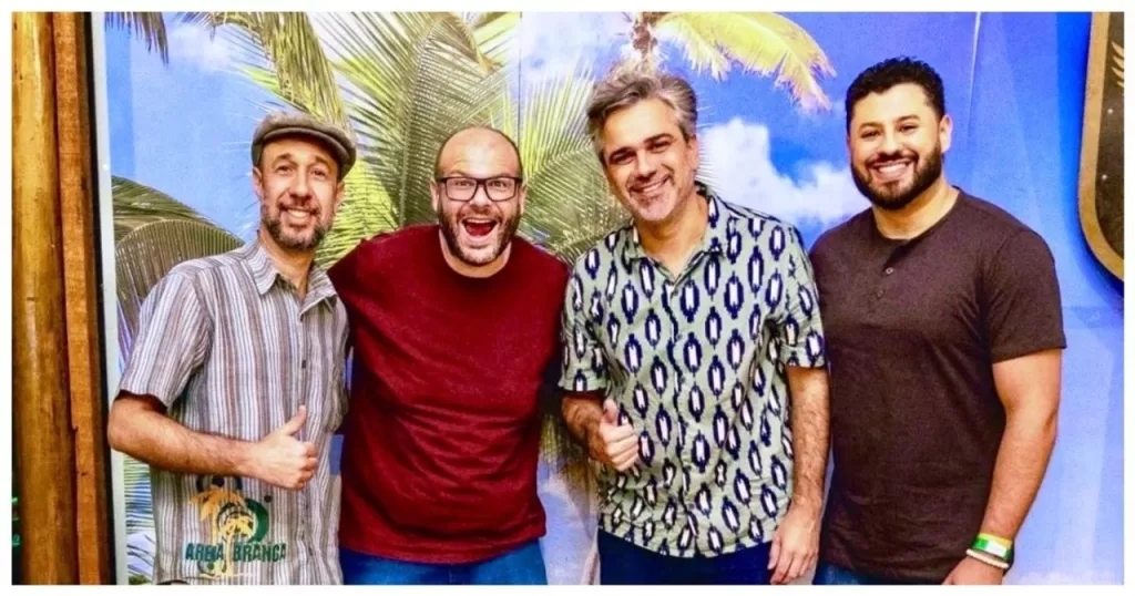 Os quatro integrantes da banda Areia Branca posam sorrindo diante de um painel colorido
