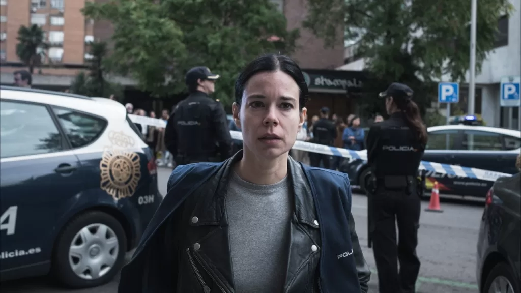 Atriz em uma rua de Madri isolada pela polícia, com viaturas ao fundo, em cena do filme Colisão Implacável