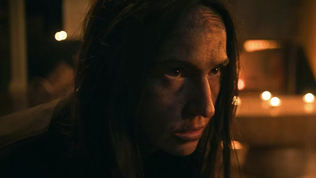 Grace Collender como Orla, com olhar assustado, em um ambiente escuro iluminado por velas