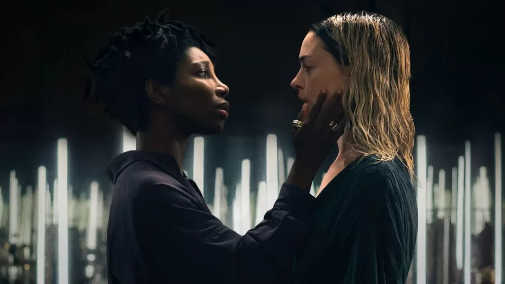 Michaela Coel e Anne Hathaway frente a frente, de rostos próximos, em um palco iluminado por velas