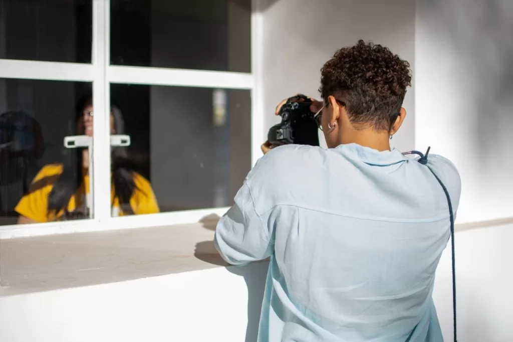 Fotógrafo registra, através de uma janela de vidro, uma mulher de camiseta amarela