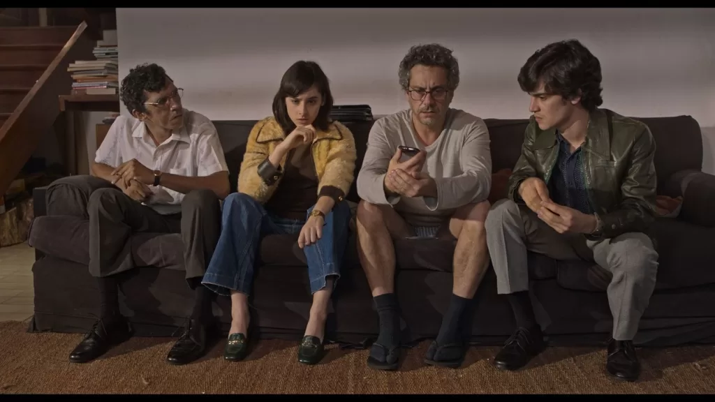 Quatro personagens sentados lado a lado em um sofá, em cena do filme Sem Pai Nem Mãe; ao centro, Alexandre Nero olha para um celular
