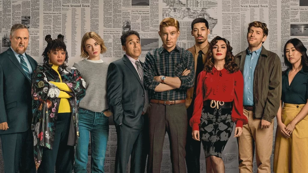 Elenco de The Paper posando lado a lado diante de uma parede coberta de páginas de jornal, em imagem de divulgação da série